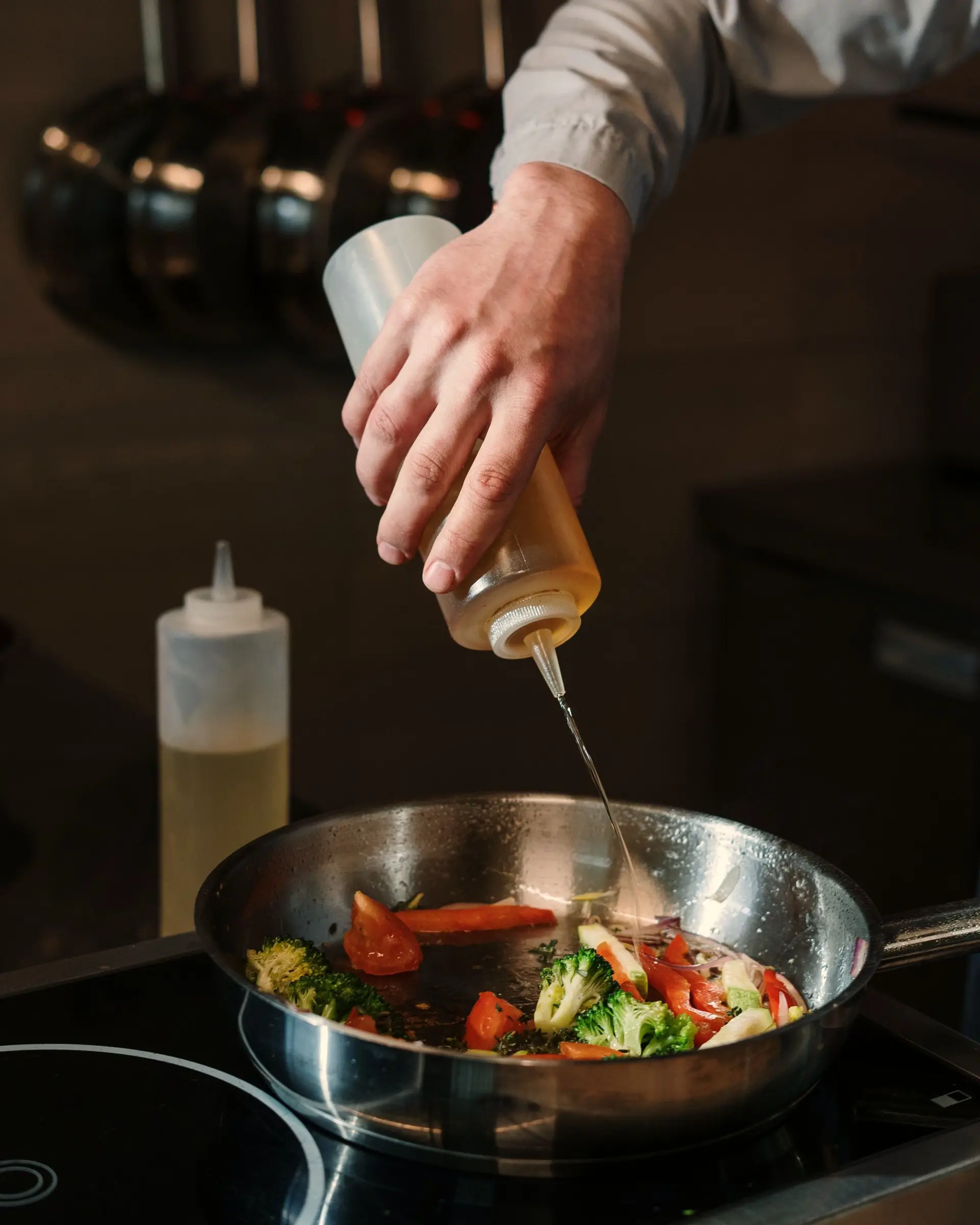Mano echando aceite en una sartén con verduras