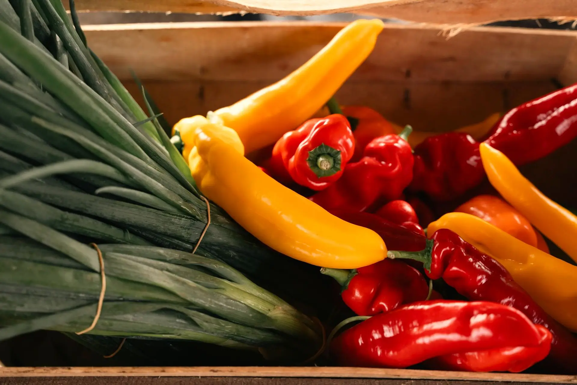 Pimientos y cebolletas en una caja de madera