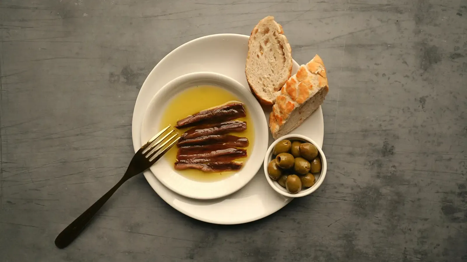 Plato de anchoas en aceite con pan de coca y aceitunas visto desde arriba